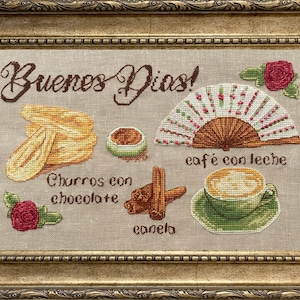 Puede incluir: Un dise&ntilde;o de bordado de punto de cruz que representa una escena de desayuno con el texto "Buenos Dias!" en espa&ntilde;ol. El dise&ntilde;o incluye churros con chocolate, una taza de caf&eacute; con leche, palitos de canela y un abanico.