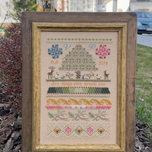 May include: Framed cross-stitch sampler with a wooden frame. The design features a central tree, floral and geometric patterns, and the text "Ars longa vita brevis est." The color palette includes shades of green, pink, blue, and beige.