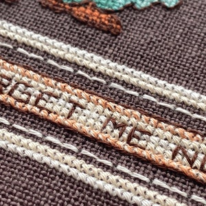Pode incluir: Close-up de um tecido marrom com costuras brancas e marrons. A palavra "FOREVER" &eacute; bordada em fio marrom.