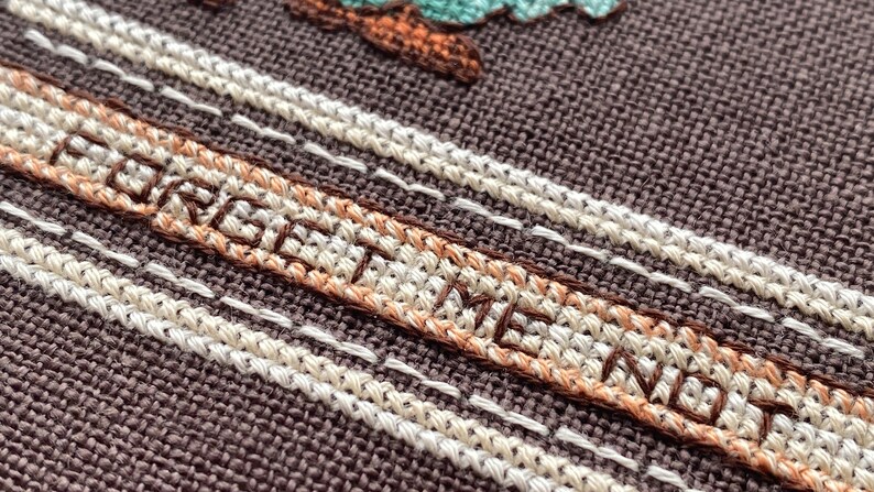 Pode incluir: Close-up de um tecido marrom com costuras brancas e marrons. A palavra "FOREVER" &eacute; bordada em fio marrom.