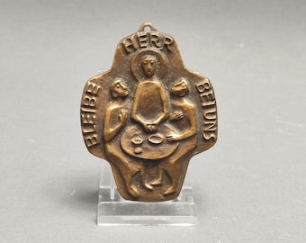 May include: A bronze cross pendant with a relief image of three figures seated at a table. The inscription "HERB BLEIBE BEI UNS" is around the edge of the cross.