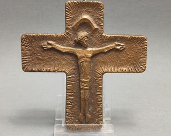 May include: A bronze crucifix with a stylized figure of Jesus Christ on the cross. The cross has a textured surface and a halo above Jesus' head.