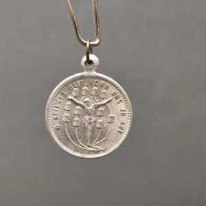 May include: A silver-colored pendant with a religious theme. The pendant features a depiction of Jesus on the cross, surrounded by text and decorative elements. The pendant is suspended from a metal clasp.