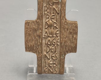 May include: A bronze cross with a textured surface and the inscription "ICH BIN BEI DIR ALLE TAGE DES LEBENS" in raised letters.