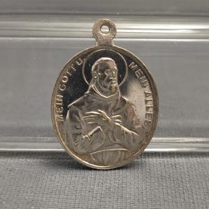 Puede incluir: Pendiente ovalado de plata con una imagen religiosa de un hombre barbudo y el texto "Mein Gott Mein Alles".