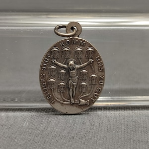 May include: Silver pendant with a religious image of Jesus Christ on the cross surrounded by 12 faces. The inscription reads "Heiliges Blut Komm Uns Zu Gut".