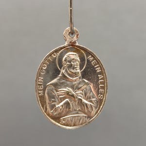 Puede incluir: Colgante ovalado de plata con un relieve detallado de un hombre barbudo con aureola. Las palabras "MEIN GOTTU" y "MEIN ALLES" están grabadas en el borde. Un pequeño lazo en la parte superior para una cadena.
