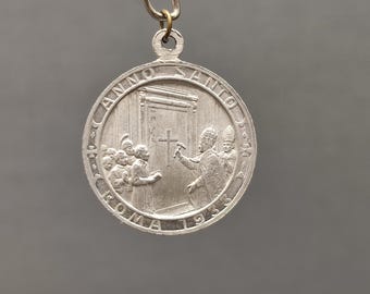 May include: A silver-colored round pendant with a religious scene. The pendant features the text "ANNO SANTO ROMA 1933" around the edge. The image depicts figures in religious attire, with a cross prominently displayed.