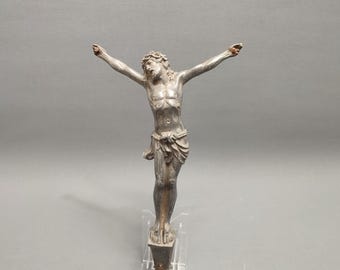 May include: A silver-toned metal sculpture of Jesus Christ on the cross. The sculpture is detailed and shows Jesus with a crown of thorns and a loincloth.