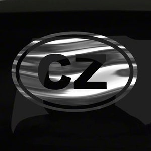May include: A black and white oval sticker with the letters "CZ" in black on a silver background. The sticker has a brushed metal effect.