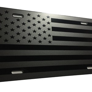 May include: A black and gray metal license plate featuring a black and white American flag design.