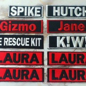 May include: A collection of eight embroidered patches with various names and phrases, including "Spike", "Gizmo", "Hutcho", "Jane", "Pole Rescue Kit", "K!W!" and "Laura". The patches are black with white or red lettering.
