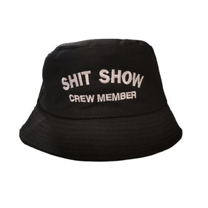 May include: Black bucket hat with white embroidered text that reads "SHIT SHOW CREW MEMBER".