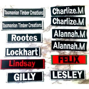 May include: A collection of black and white embroidered name tags with white lettering. The names include "Charlize.M", "Alannah.M", "Rootes", "Lockhart", "GILLY", and "LESLEY". There is also a red name tag with white lettering that says "FELIX" and two black name tags with white lettering that say "Tasmanian Timber Creations" and "Lindsay".