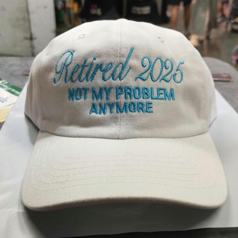 May include: White baseball cap with blue embroidered text that reads "Retired 2025 Not My Problem Anymore".