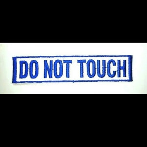May include: A white rectangular patch with a blue border and the text "DO NOT TOUCH" in blue embroidery.