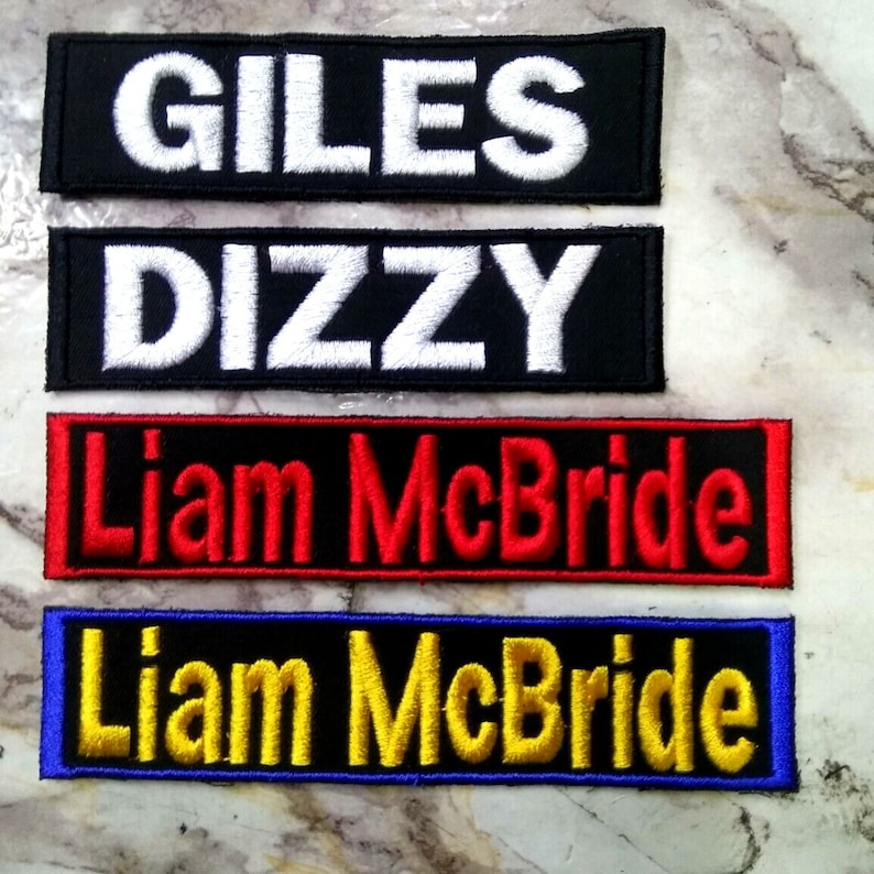 May include: Four embroidered patches with different names. The top patch is black with white text that reads "GILES". The second patch is black with white text that reads "DIZZY". The third patch is black with red text that reads "Liam McBride". The bottom patch is blue with yellow text that reads "Liam McBride".