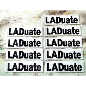 May include: Eight white fabric patches with black embroidered text that reads "LADuate".
