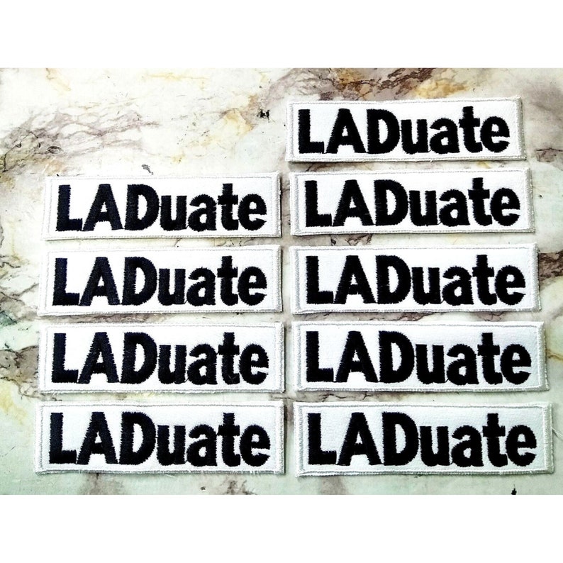 May include: Eight white fabric patches with black embroidered text that reads "LADuate".