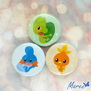 May include: Three round buttons with cartoon images of Pokemon characters. The first button is green with a green and yellow lizard-like Pokemon. The second button is blue with a blue and orange water Pokemon. The third button is beige with an orange and yellow fire Pokemon.