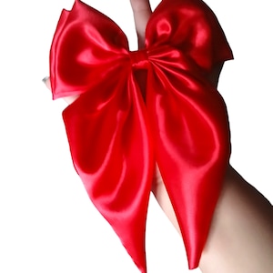 May include: A large, vibrant red satin bow. The bow is held up against a white background. The bow has a classic shape with multiple loops and long, pointed tails. The satin fabric has a glossy sheen.