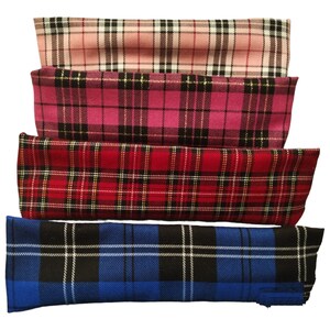 May include: Four fabric swatches stacked on top of each other. The top swatch is pink with a white and black plaid pattern. The second swatch is pink with a black and gold plaid pattern. The third swatch is red with a black and yellow plaid pattern. The bottom swatch is blue with a black and white plaid pattern.
