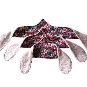 May include: Three bunny ear headbands. The headbands have a floral pattern in shades of pink, purple, and green. The inner ears are a soft, light pink. The headbands are arranged in a fan shape.