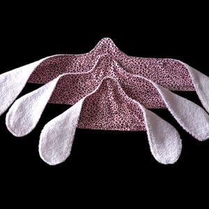 May include: Three hair towels with a pink leopard print design and white terry cloth ends are arranged against a black background. The towels are folded to create a layered effect, showcasing the contrasting textures and patterns.