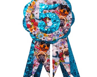 May include: A decorative rosette with a blue glitter trim and ribbons. The rosette features a collage of various dog breeds and flowers, with the number "5" in the center. The ribbons are also blue with glitter.