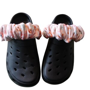Könnte beinhalten: Ein Paar schwarze Gummischuhe mit einem floralen Stoffband um die Oberseite jedes Schuhs.