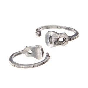 May include: Two silver-colored guitar-shaped rings. One ring is positioned with the guitar facing up, and the other is positioned with the guitar facing down. The text "Journey" is inscribed on one ring, and "Accessorizing Life" is inscribed on the other.