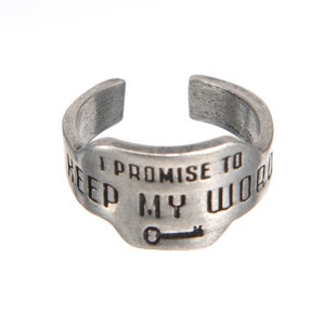 May include: A silver ring with the inscription "I promise to keep my word" and a small key symbol.