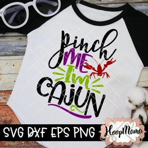 May include: White and black raglan style t-shirt with the text "Pinch Me I'm Cajun" in black, purple, and green. A red crawfish graphic is in the center. Sunglasses are in the upper left corner.