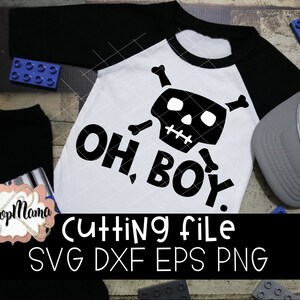 May include: A white onesie with black text that reads "Oh Boy!" and a black and white skull and crossbones design. The onesie is on a wooden surface with blue and gray toy blocks.