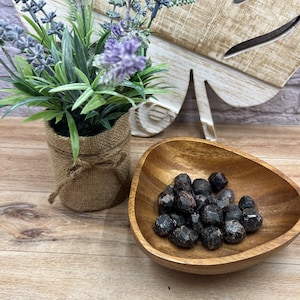May include: A wooden bowl filled with dark red garnet crystals. The bowl is sitting on a wooden surface.
