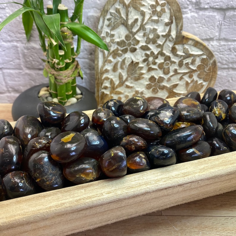 May include: A wooden bowl filled with dark amber tumbled stones. The stones are smooth and polished, with a variety of shapes and sizes.