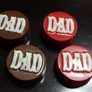 May include: Four chocolate-covered cookies with the word "DAD" written in white icing. Two cookies are brown and two are red.