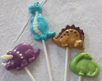 May include: Four dinosaur-shaped lollipops on sticks. The lollipops are blue, purple, brown, and green.