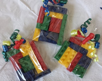May include: Three small plastic bags filled with colorful toy building blocks. The blocks are red, yellow, green, and blue. The bags are tied with colorful ribbons.