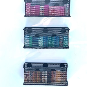 May include: Three black metal wire wall mounted storage baskets with various colorful items inside.
