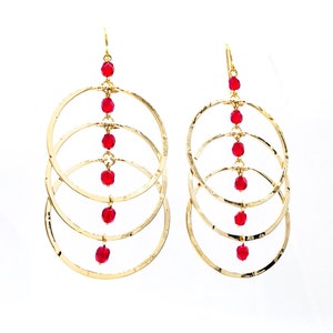 May include: Gold hoop earrings with four concentric circles and a dangling chain of red beads.