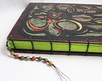 Journal with coptic binding in deep shades of red and green with lime green accent on binding and multicolor bead dangle