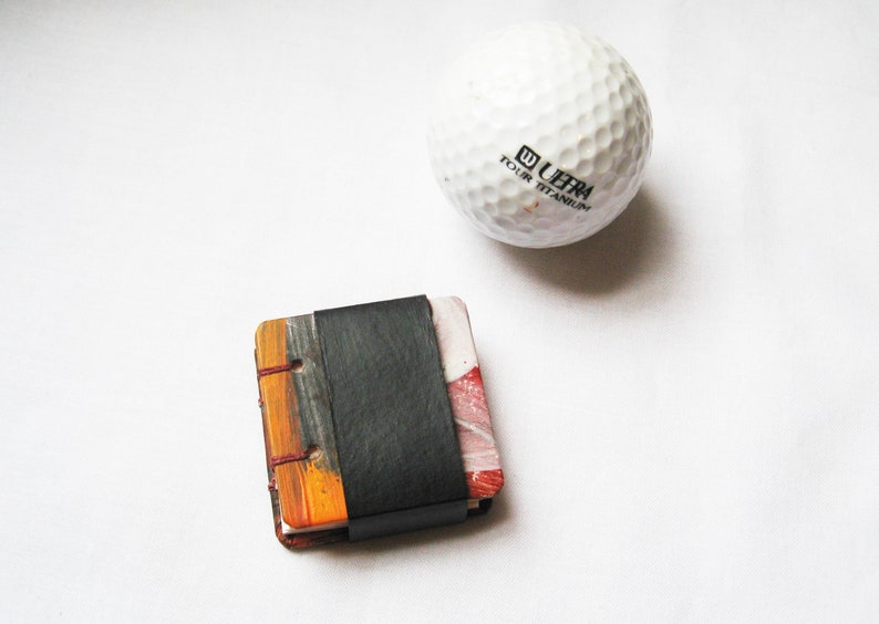 Pu&ograve; includere: Un piccolo libro fatto a mano con una copertina in pelle nera e pagine dipinte colorate. Il libro &egrave; delle dimensioni di una palla da golf.