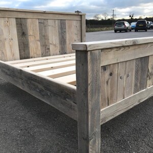 Puede incluir: Un marco de cama de madera r&uacute;stica con un cabecero hecho de tablones de madera recuperados. El marco est&aacute; hecho de madera natural con un acabado gris claro. La cama est&aacute; sobre una superficie de asfalto gris.