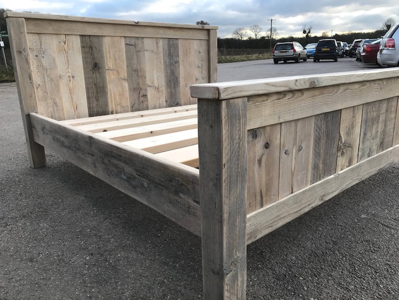 Puede incluir: Un marco de cama de madera r&uacute;stica con un cabecero hecho de tablones de madera recuperados. El marco est&aacute; hecho de madera natural con un acabado gris claro. La cama est&aacute; sobre una superficie de asfalto gris.