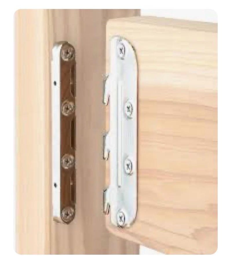 Op de afbeelding: Een metalen bedrailbeugelset bestaande uit twee zilverkleurige stalen platen bevestigd aan lichtgekleurde houten planken. De ene plaat is voorzien van drie naar beneden gerichte haken, terwijl de andere plaat bijbehorende sleuven heeft.