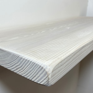 May include: White wooden shelf with a smooth, slightly rounded edge. The shelf is made of natural wood with visible grain and has been painted white.