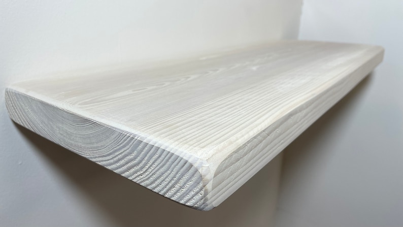 May include: White wooden shelf with a smooth, slightly rounded edge. The shelf is made of natural wood with visible grain and has been painted white.