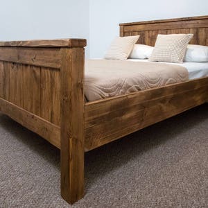 Puede incluir: Un marco de cama de madera r&uacute;stico con un acabado marr&oacute;n natural. La cama tiene una cabecera y un piecero con un dise&ntilde;o de listones. La cama est&aacute; hecha de madera recuperada y tiene un estilo sencillo y de granja.