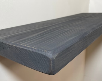 Puede incluir: Una estantería de madera gris oscuro con un borde redondeado. La estantería está hecha de madera natural y tiene un aspecto rústico.